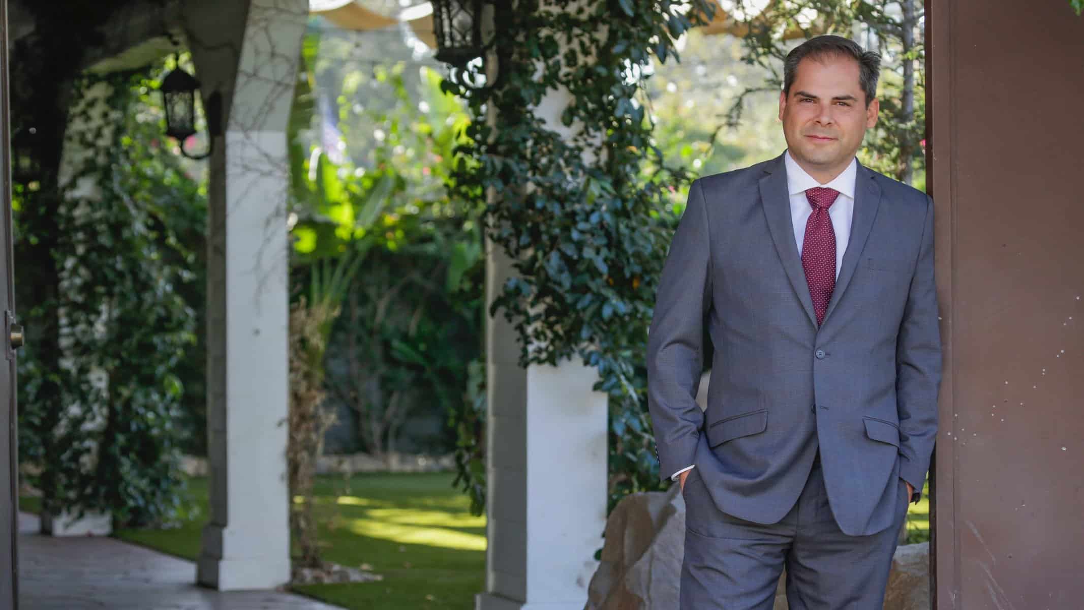 Mike Garcia wearing a grey suit smiling with a garden behind him.