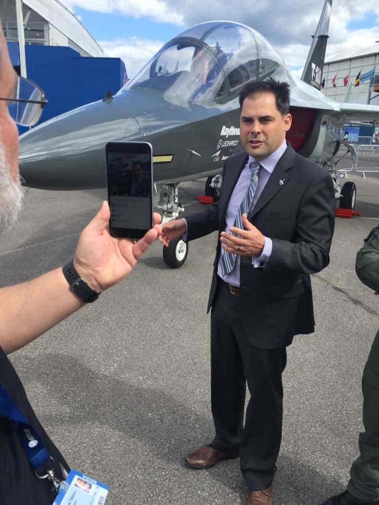Mike Garcia standing in front of a jet being filmed by a phone.